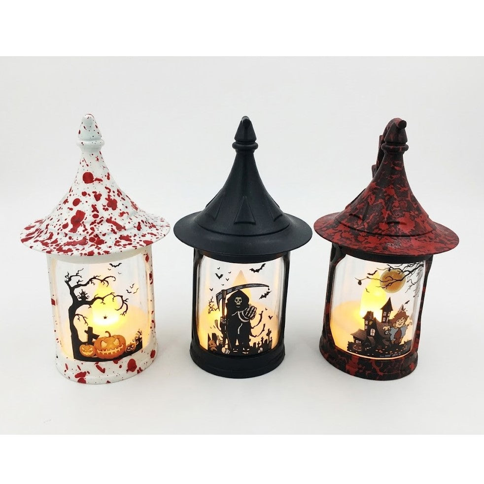Three Halloween witch-house lanterns with pointed roofs, shown side by side on a white background. The left lantern is white with red splatter and a pumpkin-and-tree design, the middle lantern is black with a skeleton-and-horror scene, and the right lantern is dark red with a haunted-house design.