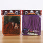 Two packaged Halloween creepy cloth decorations on a wooden surface against a white background. The left package contains an orange spooky fabric with a skeletal hand reaching out, and the right package contains purple cobweb-like draped cloth over a coffin prop.