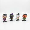 Four small Halloween-themed wind-up toy figurines lined up on a white background: a witch, a black cat, a ghost, and a jack-o'-lantern.