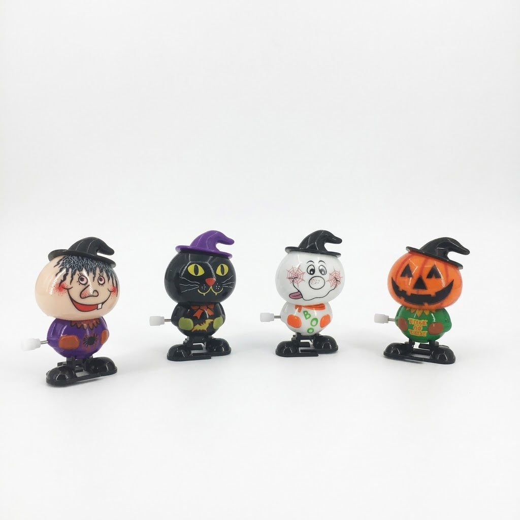Four small Halloween-themed wind-up toy figurines lined up on a white background: a witch, a black cat, a ghost, and a jack-o'-lantern.