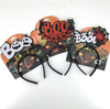 Three Halloween headbands on retail hangers. One headband has a red glittery 'BOO' sign with black spiderwebs and black cat silhouettes.
