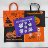 Four Halloween-themed fabric tote bags arranged on a white background: orange with black handles and spooky graphics, black with orange handles and 'Happy Halloween' text, purple with white ghost cutouts and 'Happy Halloween' text, and orange with black handles, jack-o'-lantern graphics, and 'Happy Halloween' text.