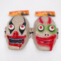 Two plastic Halloween clown masks with attached retail hangers, shown side by side on a plain white background. One mask is beige with black eye makeup, red nose, and red mouth details; the other is beige with green eye makeup and red mouth details.