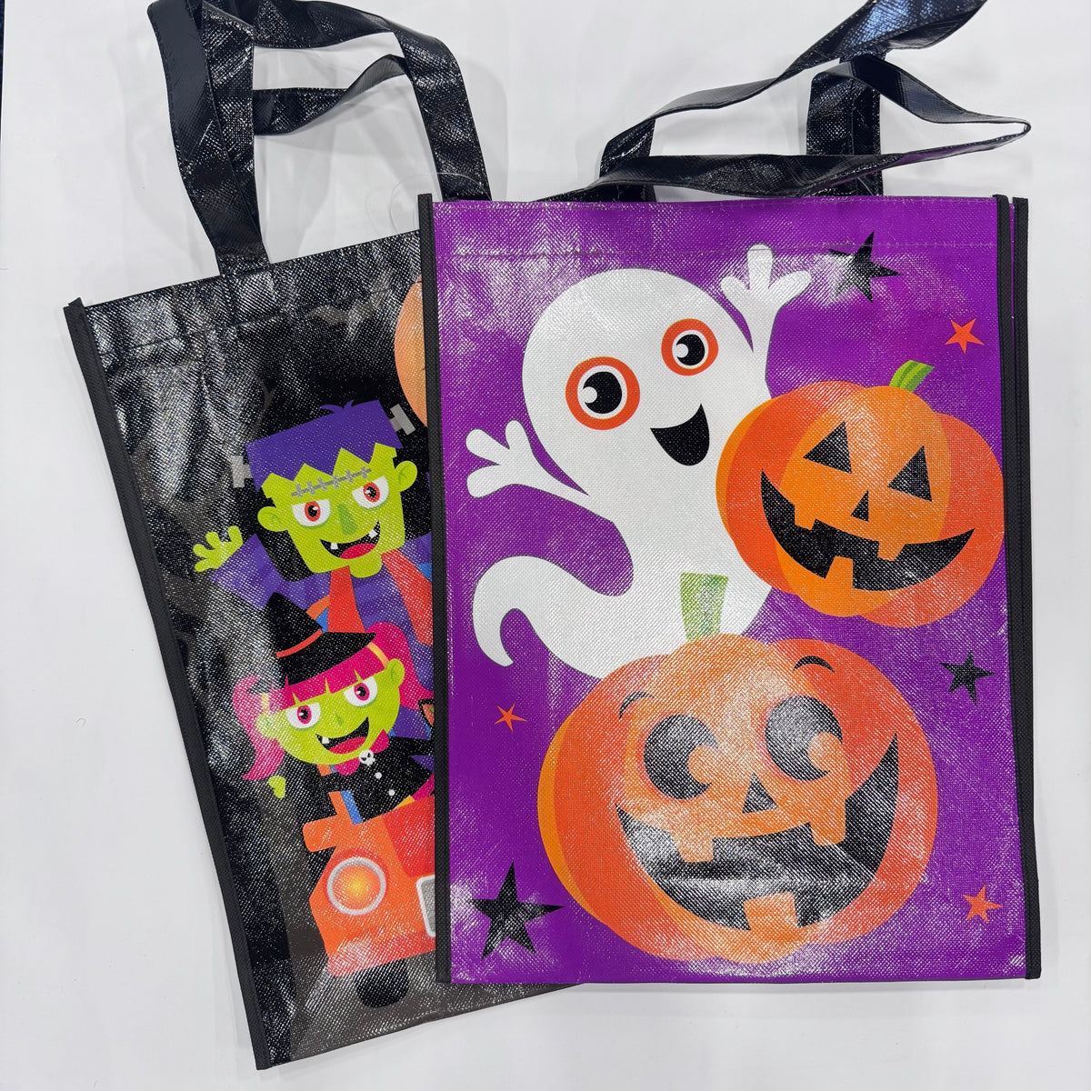 Two reusable Halloween candy bags on a white background. The front bag is purple with a white ghost, orange jack-o'-lanterns, and small black stars.