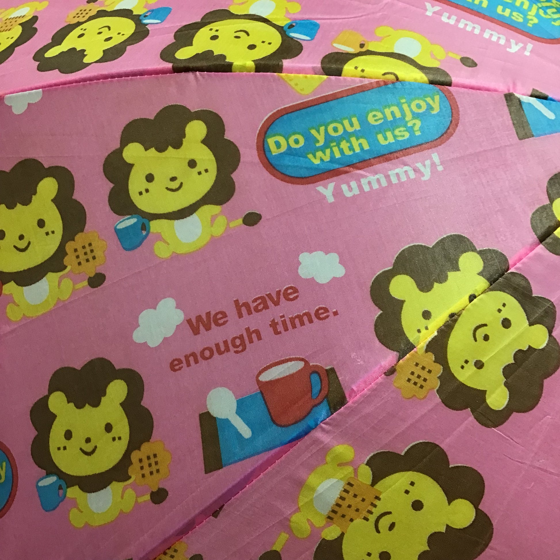 Pink umbrella with cartoon lion designs and text on a pink background