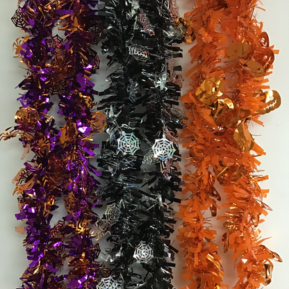 Three metallic tinsel garlands with spiderweb and leaf decorations, shown in purple and bronze, black, and orange, laid side by side on a white background.