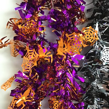 Halloween tinsel garland with purple and orange metallic spider web and spider cutout decorations, shown alongside a black and silver version on a white background.