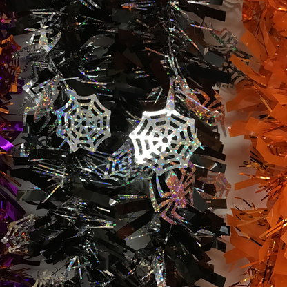 Holographic spider and web Halloween decorations hanging on a black tinsel tree, with orange tinsel visible on the right side.